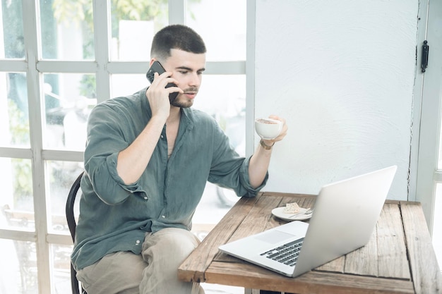 Bel giovane uomo d'affari che lavora al computer portatile e lavora online mentre si siede al tavolo della caffetteria uomo d'affari che lavora all'aperto vista laterale