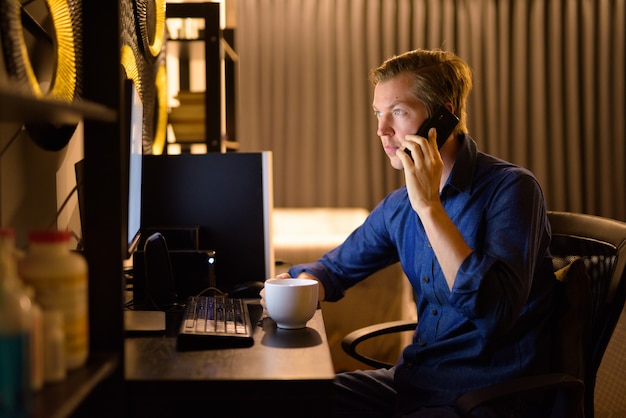 Bel giovane uomo d'affari con caffè parlando al telefono mentre si lavora da casa