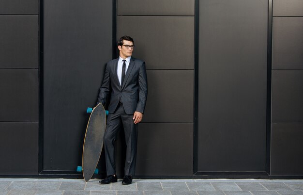 Bel giovane uomo d'affari con il suo longboard moderno