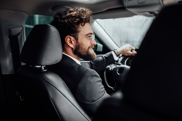 Bel giovane uomo d'affari in abito completo che sorride mentre guida una nuova auto