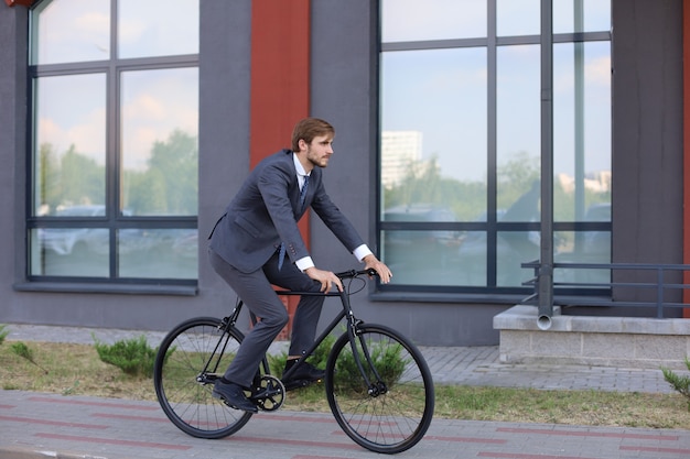 Bel giovane uomo d'affari in sella alla sua bicicletta in città. Concetto di trasporto ecologico.