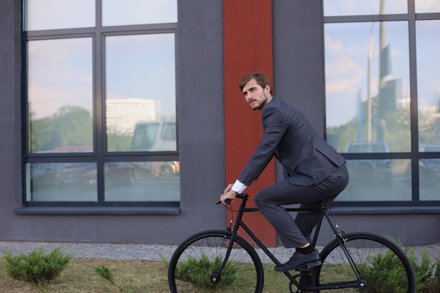 Bel giovane uomo d'affari in sella alla sua bicicletta in città. Concetto di trasporto ecologico.