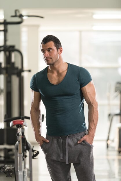 Bel giovane uomo in piedi forte in maglietta verde e flettendo i muscoli Muscoloso atletico culturista modello di fitness in posa dopo gli esercizi