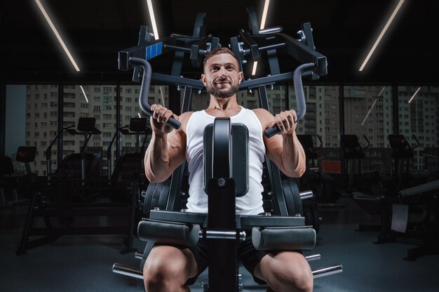 Bel giovane uomo pompa le spalle in una macchina speciale. Concetto di fitness e bodybuilding.