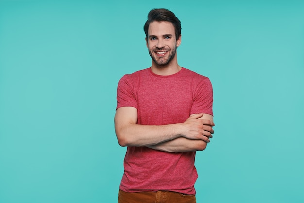 Bel giovane uomo sorridente in abbigliamento casual che guarda la macchina fotografica e tiene le braccia incrociate