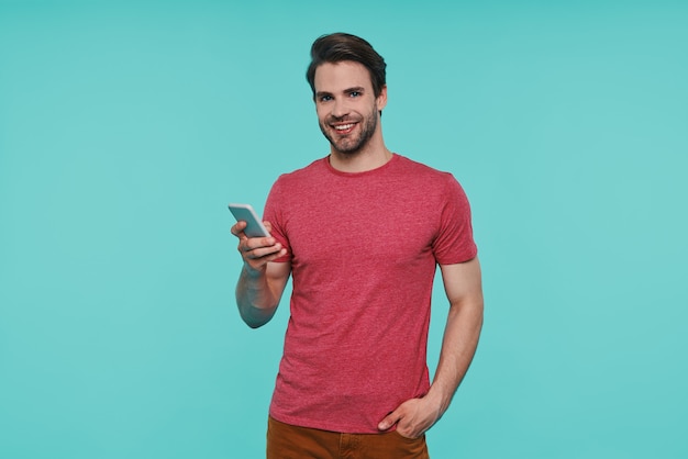 Bel giovane uomo sorridente in abbigliamento casual che tiene in mano uno smartphone