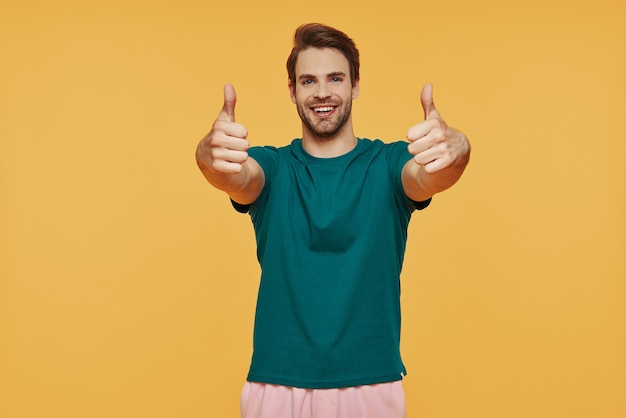 Bel giovane uomo sorridente in abbigliamento casual e gesticolando in piedi contro il muro giallo