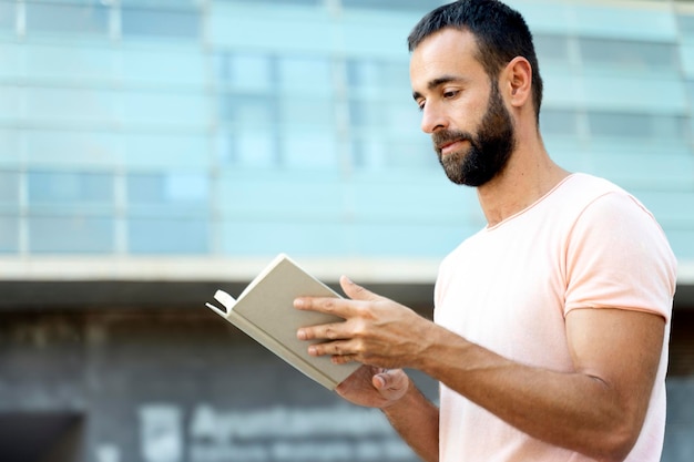 Bel libro di lettura uomo barbuto pensieroso in piedi sulla strada, copia spazio. Studente che studia