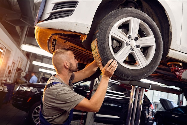 Bel meccanico di automobili installa e ispeziona le ruote dell'auto