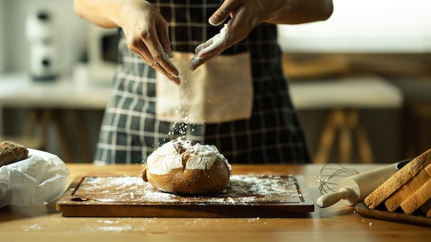 Bel momento del fornaio che indossa il grembiule che setaccia la farina sull'impasto facendo il pane in cucina