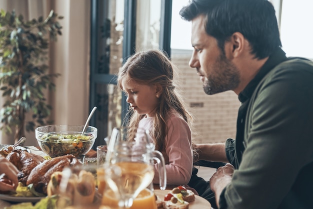 Bel padre e sua figlia seduti al tavolo da pranzo mentre mangiano insieme