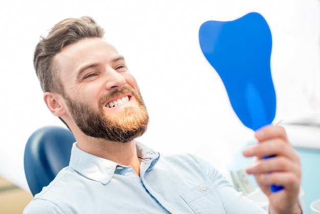 Bel paziente maschio che guarda il suo bel sorriso seduto nello studio dentistico