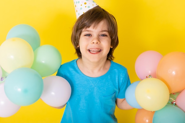 Bel ragazzino di compleanno in camicia blu e cappello con palloncini sfondo giallo buon compleanno