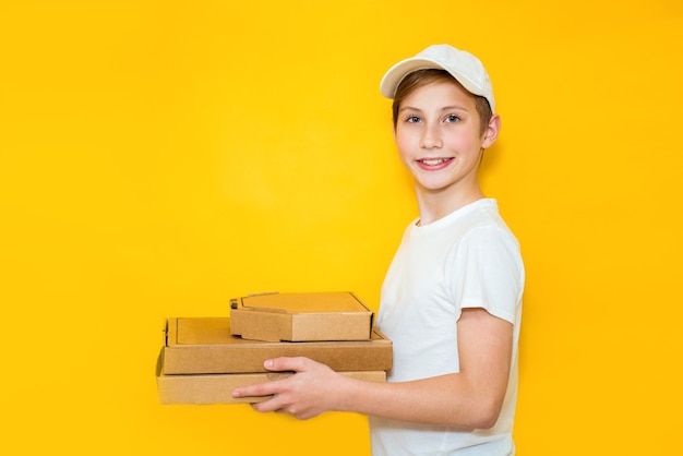 Bel ragazzo adolescente con una pila di scatole per pizza su uno sfondo giallo. Lavora nel concetto di infanzia