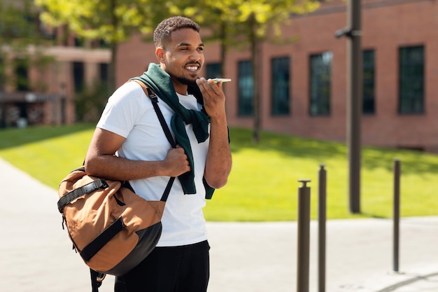 Bel ragazzo afroamericano che registra un messaggio audio sul cellulare che cammina nella copia dell'area urbana della città