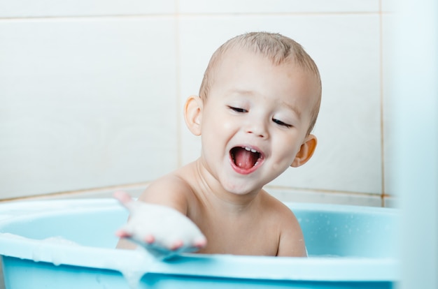 Bel ragazzo che fa il bagno a un bambino nella vasca pulita e igienica, guarda la mano che è nella schiuma