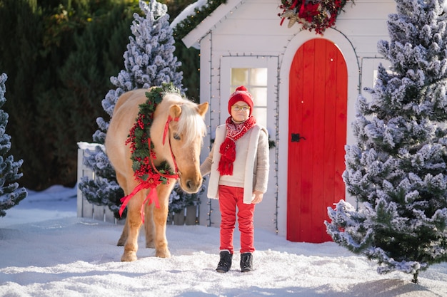 Bel ragazzo con gli occhiali e pony adorabile con ghirlanda festiva vicino alla piccola casa me