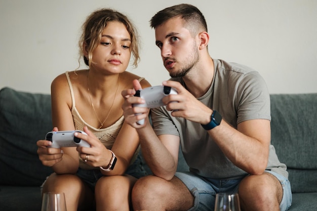 Bel ragazzo con la sua fidanzata che gioca ai videogiochi usando i joystick, l'uomo insegna alla sua ragazza come fare