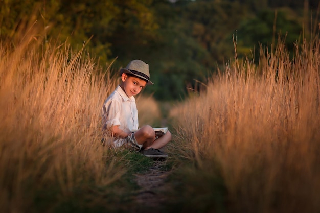 Bel ragazzo con un cappello si siede su una strada di campagna