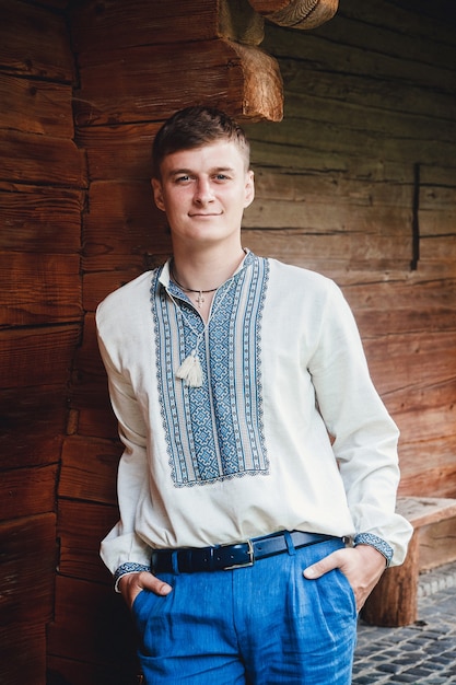 Bel ragazzo con una camicia ricamata sullo sfondo di una casa in legno.