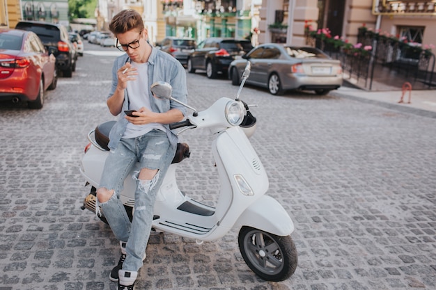 Bel ragazzo è seduto sulla moto e tenendo in mano il telefono