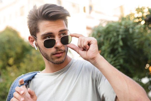 Bel ragazzo giovane camminare all'aperto ascoltando musica in strada alla ricerca da parte