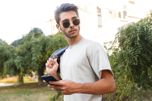 Bel ragazzo giovane camminare all'aperto ascoltando musica in strada utilizzando il telefono cellulare e chiacchierando