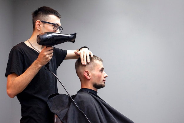 Bel ragazzo ha un taglio di capelli in un barbiere un barbiere kazako asciuga l'asciugacapelli di un cliente