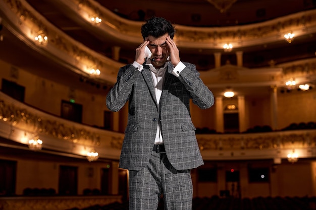 Bel ragazzo in abito classico elegante sta cercando di pensare a qualcosa in piedi sul palco durante l'esibizione, parlare discorso. Ragazzo americano sul palco. Emozioni umane, leadership, concetto di performance