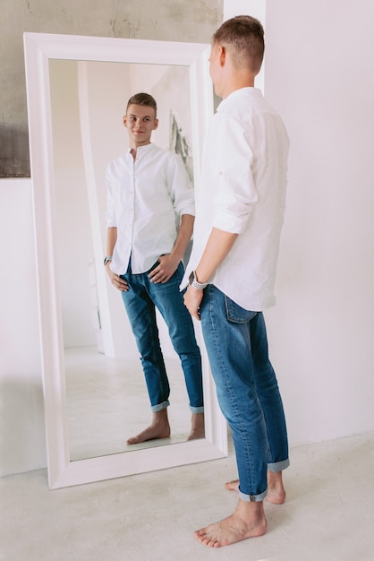 bel ragazzo in camicia bianca e jeans blu in piedi vicino allo specchio