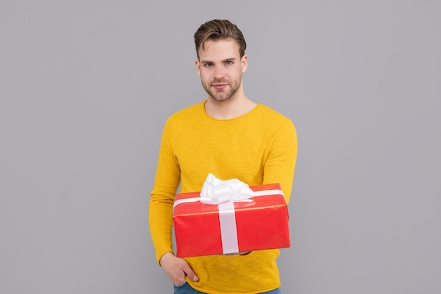 Bel ragazzo in maglione giallo tenere scatola regalo sfondo grigio, gifting.