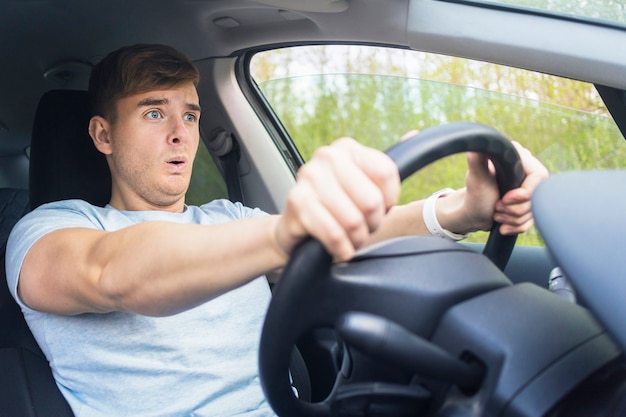 Bel ragazzo spaventato spaventato, autista, giovane uomo spaventato scioccato per avere un incidente stradale, guida auto su strada tenendo il volante dell'automobile. Non allentato da una cintura di sicurezza. Violazione del traffico