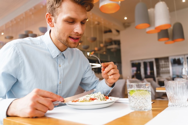 Bel signore seduto al tavolo e mangiare una deliziosa insalata fresca al bar