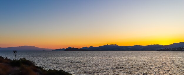 Bel tramonto sulla costa mediterranea con isole e pietre di montagne sulla spiaggia illuminate da