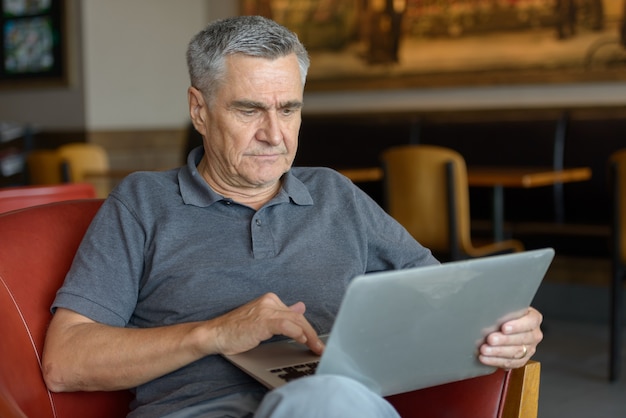 Bel uomo anziano utilizzando laptop e rilassarsi a casa al chiuso