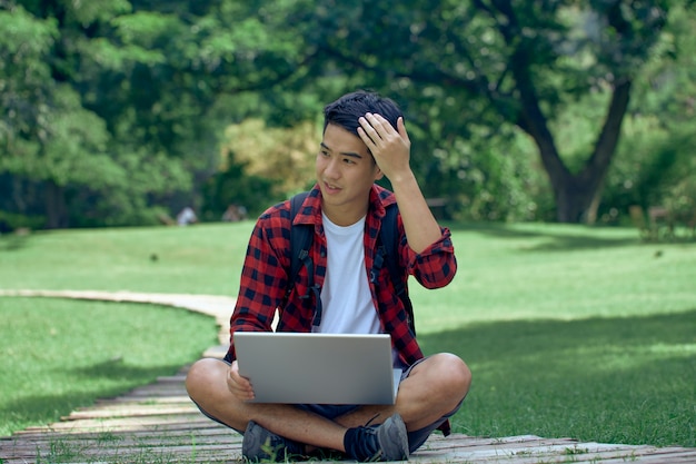 Bel uomo asiatico seduto in un giardino utilizzando un computer portatile