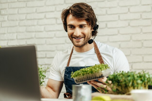 Bel uomo barbuto vende germogli di piante e piantine online utilizzando il computer portatile