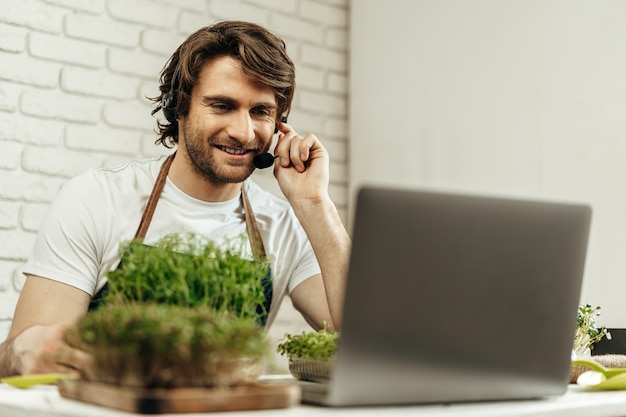 Bel uomo barbuto vende germogli di piante e piantine online utilizzando il computer portatile