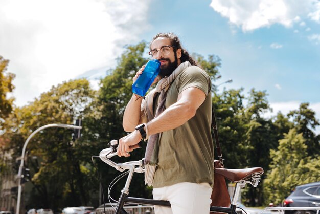 Bel uomo felice in piedi vicino alla sua bicicletta mentre beve l'acqua