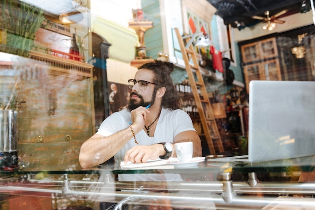 Bel uomo premuroso che tiene una penna mentre prende appunti nella caffetteria