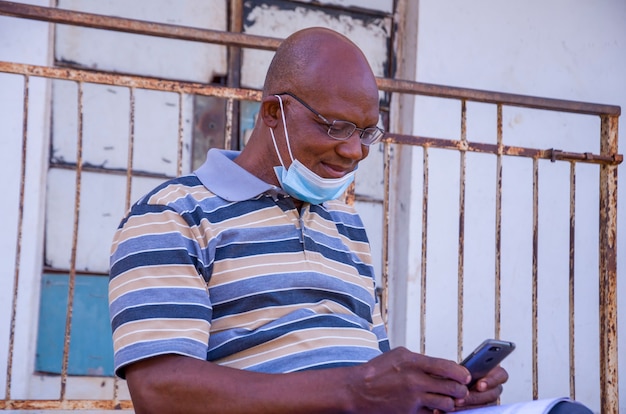 Bel vecchio africano che indossa una maschera facciale mentre usa il suo telefono.