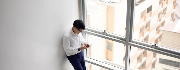 Bell'impiegato che tiene il cellulare in mano chatta con la fidanzata tramite cellulare al balcone dell'ufficio modren in momenti di relax