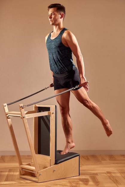 Bell'istruttore maschio di pilates che esegue esercizi di fitness per l'equilibrio di stretching su piccole attrezzature a botte presso lo studio di pilates moderno interno interno