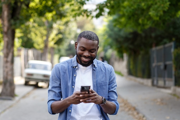 Bell'uomo afro-americano utilizza lo smartphone e sorridente