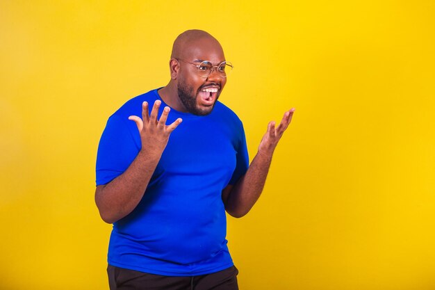 Bell'uomo afro brasiliano che indossa occhiali camicia blu su sfondo giallo Primo piano chiuso photoxACelebrando sorpreso sorpreso wow successo gioia mani aperte stupito urlando di gioia