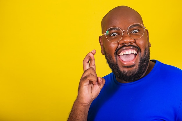 Bell'uomo afro brasiliano che indossa occhiali camicia blu su sfondo giallo segno fortunato tifo augurando voler vibrare fortuna buona fortuna disegnare