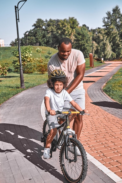 Bell'uomo afroamericano che insegna al suo bambino carino ad andare in bicicletta in una giornata di sole