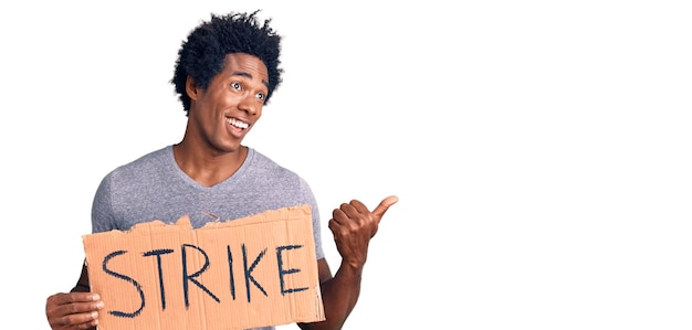 Bell'uomo afroamericano con i capelli afro che tiene il cartone dello striscione di sciopero che punta il pollice verso l'alto sorridendo felice con la bocca aperta