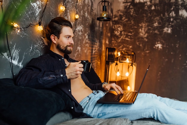 Bell'uomo al mattino, sdraiato sul letto con tablet e tazza di caffè.