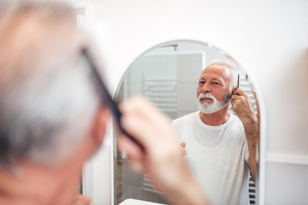 Bell&#39;uomo anziano che si pettina i capelli in bagno. Concentrati sul riflesso nello specchio.